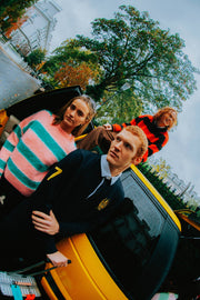 Three people standing next to a yellow car with a cityscape in the background